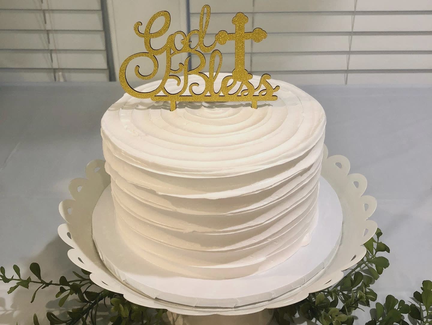 White frosted cake with ‘God Bless’ topper, perfect for religious celebrations or special events.