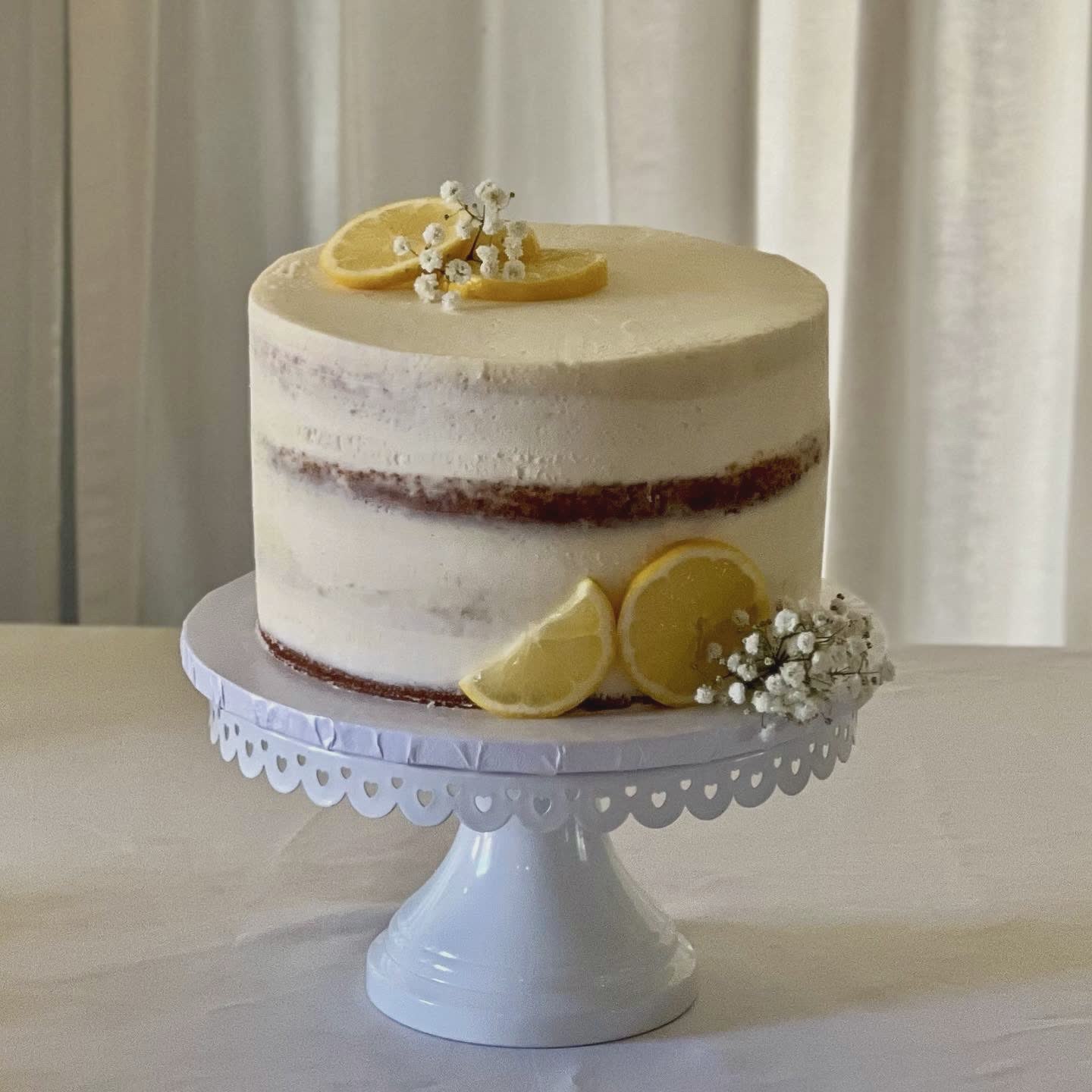 Semi-naked lemon cake topped with fresh lemon slices and baby’s breath flowers, perfect for summer events.